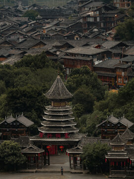 View of a pagoda-style structure amidst a dense, traditional village with dark, wooden roofs and lush green trees, Xijiang, Guizhou, China.