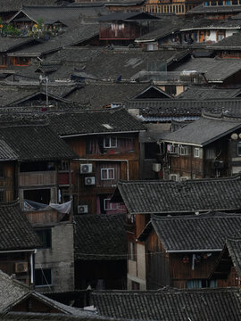View of tightly packed traditional wooden houses with dark tiled roofs create an intricate tapestry, air conditioning units contrasting with the old architecture, Xijiang, Guizhou, China.