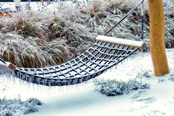 Frozen rope hammock with icicles hanging in winter snow covered garden