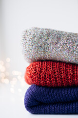 Stack of red, blue and shiny sweaters with Christmas bokeh lights.