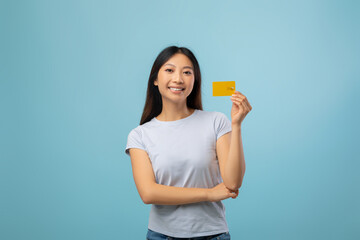 A young woman with long black hair stands against a light blue background, holding up a yellow card with a smile on her face. She appears cheerful and confident.