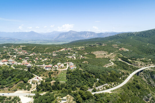 Aerial view of the winding roads and verdant hillsides meet the distant mountains under the bright sky, Fanari, Preveza, Greece.
