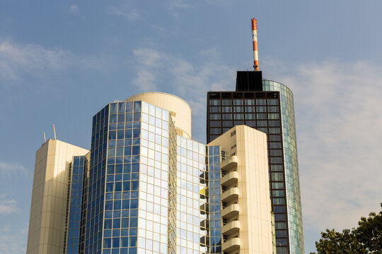 View of modern architecture featuring glass and concrete skyscrapers reaching towards the blue sky, contrasting sharp lines against softer clouds, Frankfurt am Main, Hessen, Germany.