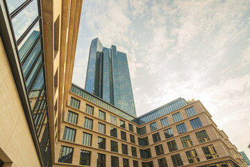 View of modern architecture with towering glass skyscraper rising above symmetrical beige buildings under a blue sky streaked with clouds, Frankfurt am Main, Hessen, Germany.