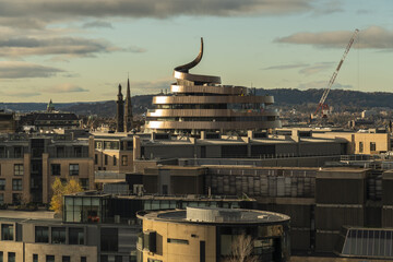 View of a winding, modern architectural marvel gleams against a vast urban landscape, its metallic curves reflecting the sky, a contrast to the historic buildings, Edinburgh, Scotland, United Kingdom.