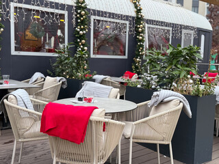 Outdoor cafe terrace decorated for Christmas with blankets and lights. Winter leisure space, seasonal hospitality and festive urban atmosphere