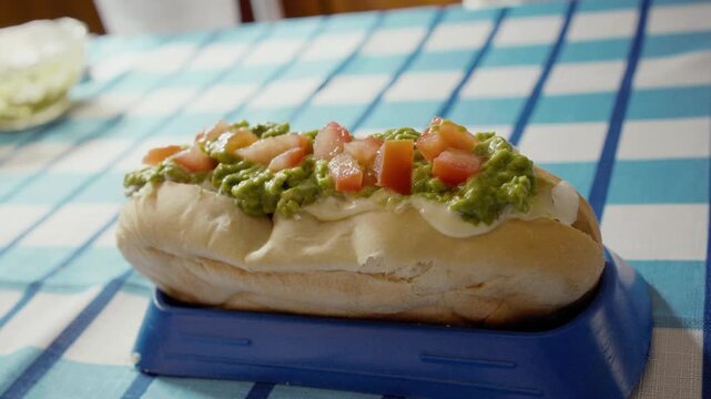 Vibrant Chilean Completo Hot Dog with Fresh Avocado and Mayonnaise Drizzle, Close-up of South American Comfort Food: The Overloaded Completo Sandwich