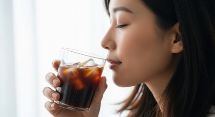 Young asian woman enjoying a refreshing iced coffee drink by a bright window