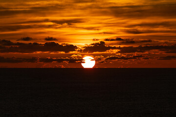 Scenery of vibrant sunset with clouds over the horizon of dark sea.