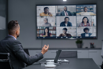 A person is engaged in a video call with multiple participants displayed on a large screen. Each...