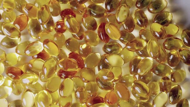 Top-down, close-up video of golden softgel capsules, like vitamin or fish oil supplements, slowly rotating on a turntable on white background showing concepts of healthcare, medicine, and nutrition.