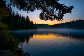 A tranquil lakeside scene captures the calming beauty of a sunset, with mist rising off the water and trees framing the view, evoking feelings of peace and reflection.
