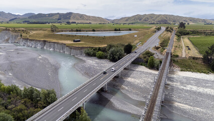 Aerial view of the State Highway 1 bridge cutting across the braided river near the railway, a contrast of grey riverbed against the green fields, Seddon, Marlborough Region, New Zealand.