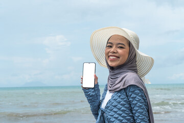 A young woman holding a mobile phone on a beautiful beach in the afternoon, the theme of vacation, promotion and nature tourism.