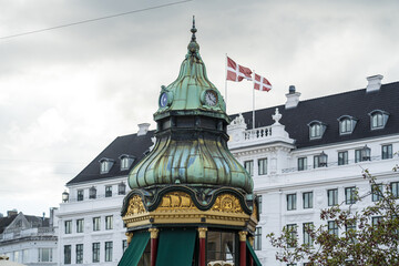 View of the copper-green tower with golden ornaments, a clock, and a Danish flag waving against a white building, Indre By, Copenhagen, Denmark.