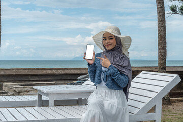 a young woman holding a cell phone in a hotel with a beach view while on vacation, perfect for vacation promotions and social media