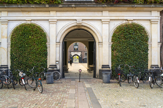 View of the textured archway framed by lush greenery and parked bicycles, inviting passage into the city, Indre By, Copenhagen, Denmark.