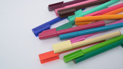 Fototapeta premium Close up of various multi colored markers scattered randomly on a white background, useful for stationery and education themes