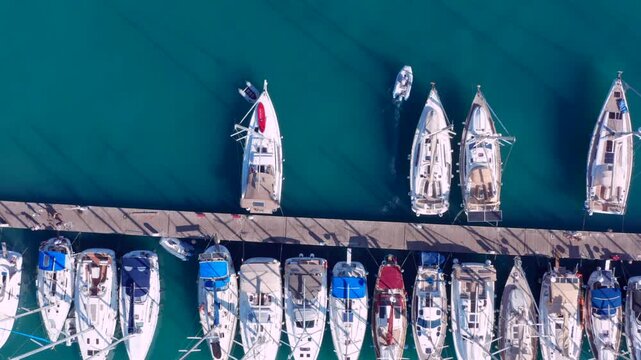 Overhead top down view of sailboats docked in orderly rows large marina green water many ships. neatly docked along symmetrical wooden pier Greece. Small motorboat 
