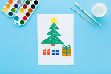 Drawn green Christmas tree with colorful gift boxes on white paper on light blue table background. Pastel color. Little child handcraft. Closeup. Flat lay. Top down view.