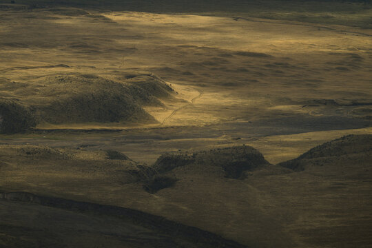 View of sun-kissed, rolling plains dotted with shadowed hills and a meandering trail under a soft, diffused light, Latacunga, Cotopaxi, Ecuador.