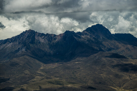 View of dramatic mountain ridges under a brooding sky, casting long shadows across the rugged terrain in Cotopaxi National Park, Latacunga, Cotopaxi, Ecuador.
