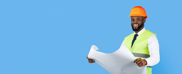 A smiling construction professional wearing a yellow hard hat and a reflective vest holds a set of blueprints. The bright blue background emphasizes the focused activity of reviewing plans.