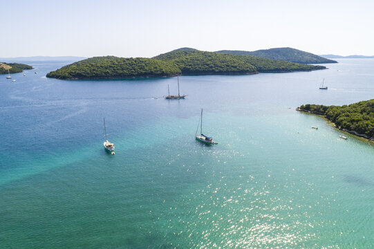 Aerial view of sailboats gliding on the turquoise waters near verdant islands under the clear sky, Syvota, Thesprotia, Greece.
