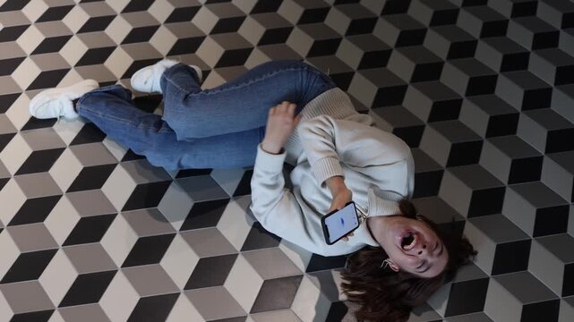 ChatGPT sparks uncontrollable laughter as young woman lies on the floor rolling from joy after funny conversation creating playful relaxed mood and emotional connection