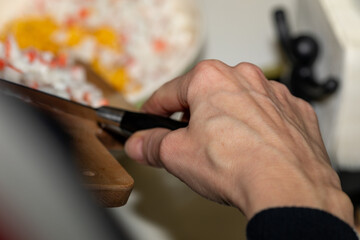 Obraz premium Close-up of a hand adding chopped crab sticks from a wooden board to a salad bowl. Authentic home cooking process with selective focus on the action.