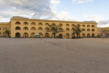 View of a grand, yellow building with arched openings under a cloudy sky, standing proudly in a spacious courtyard, Ehrenbreitstein, Koblenz, Germany.