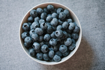 White bowl full of sweet ripe blueberries view from above, flatlay. Fresh berries in summer are natural source of vitamins and microelements. Healthy eating closeup, vegetarian diet