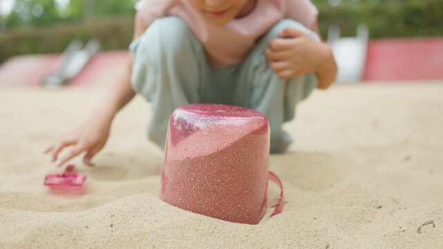 A girl plays in a sandbox on a playground in a park
