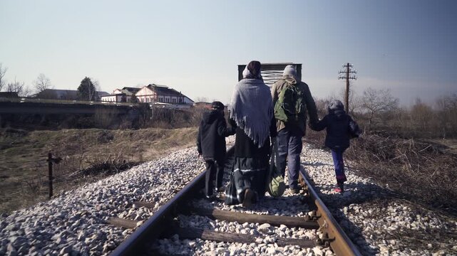 An immigrant family travels on foot by railroad tracks through the rural area, a steady shot