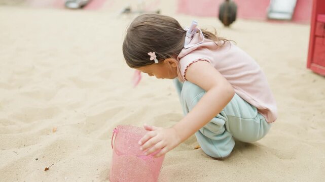 A girl plays in a sandbox on a playground in a park