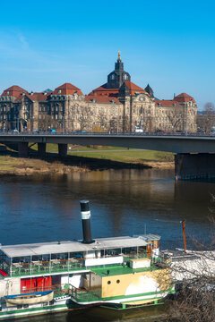 View of a vintage paddle steamer moored on the Elbe River, with a bridge and historic buildings under a clear blue sky in Dresden, Saxony, Germany.
