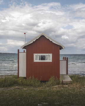 View of a striking red beach hut stands boldly against the soft, muted hues of the sea and sky, a quaint beacon on the tranquil shore, Badehuse ved Vestre Strandvej, Ero Municipality, Denmark.