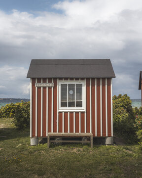 View of a striking red and white striped bathing hut stands proudly on a vibrant green lawn under a cloudy sky, Badehuse ved Vestre Strandvej, Ero Municipality, Denmark.