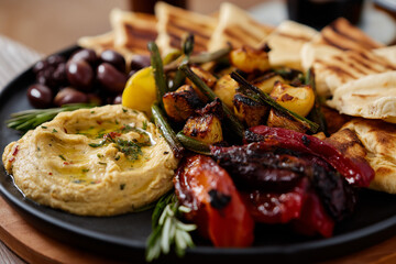 An appetizing Mediterranean platter featuring grilled vegetables, olives, and hummus, served on a round black plate, perfect for sharing at gatherings or enjoying alone.