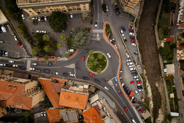Aerial view of a vibrant roundabout buzzing with cars and surrounded by terracotta rooftops and lush greenery, Imperia, Liguria, Italy.