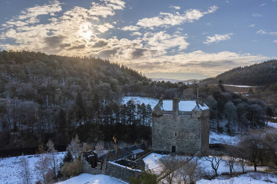 Aerial view of the stark, snow-dusted Neidpath Castle standing proud against the backdrop of frosty woodland, where the winter sun casts long shadows, Peebles, Scotland, United Kingdom.