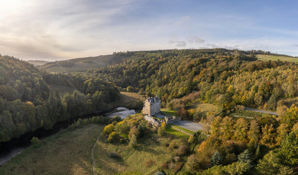 Aerial view of a medieval castle standing resolute amidst a vibrant tapestry of autumn foliage, bordering the tranquil, winding river, Peebles, Scotland, United Kingdom.