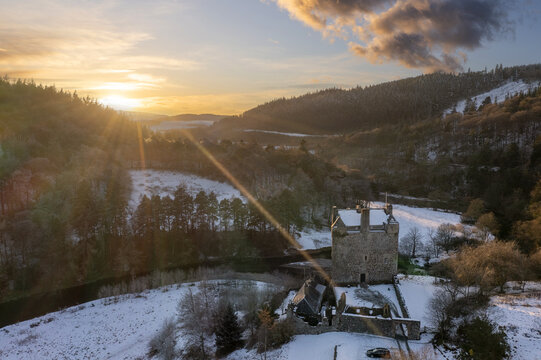Aerial view of the historic Neidpath Castle nestled in a snow-dusted landscape, bathed in the warm glow of the setting sun, Peebles, Scotland, United Kingdom.