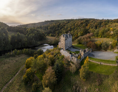 Aerial view of the historic Neidpath Castle standing proudly on a hill, surrounded by vibrant autumn foliage with the River Tweed snaking nearby, Peebles, Scotland, United Kingdom.