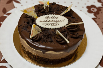 Chocolate birthday cake on white plate on brown patterned tablecloth