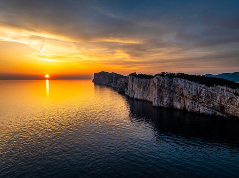 Aerial view of the sun kissing the horizon, casting a golden glow upon the tranquil sea and rugged cliffs, Sali, Zadarska Zupanija, Croatia.
