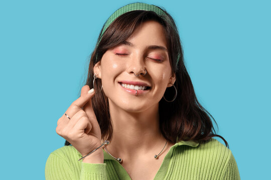 Happy young woman with face piercing on blue background