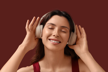 Naklejka premium Happy young woman in headphones with nose and lip piercing on dark red background