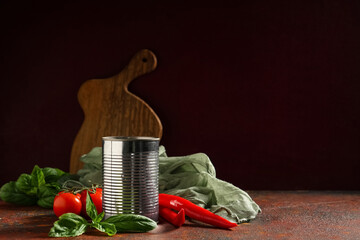 Tin can of tasty tomato paste with basil leaves and chili peppers on dark background