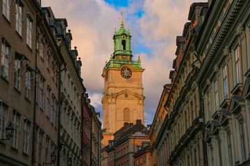 Fototapeta premium Clock tower of the Church of St Nicholas, behind a historic street of colourful buildings in the old town Gamla Stan, Stockholm, Sweden.